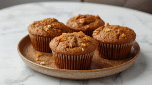 A plate of moist banana carrot muffins, golden brown, with bits of carrot and banana.