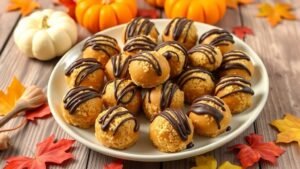 No bake pumpkin cheesecake balls coated in graham cracker crumbs and drizzled with chocolate, displayed on a plate with autumn decorations.