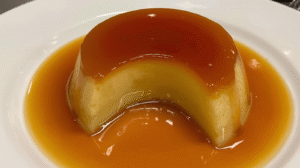 Golden leche flan topped with shiny caramel sauce, sliced to reveal creamy texture inside.
