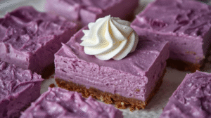 Purple ube cheesecake bars sliced cleanly to show creamy texture, topped with light whipped cream.