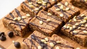 Nut-free chocolate sunflower-seed protein bars drizzled with chocolate and sprinkled with seeds on a wooden board.