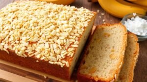 Toasted coconut pineapple banana bread loaf with slices showing moist texture, surrounded by bananas and coconut.